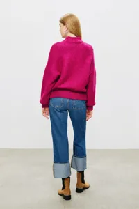 Back view detail of a vibrant pink turtleneck knitted sweater paired with cuffed denim jeans.