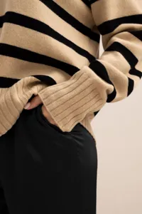 Close-up detail of beige black striped knit sweater sleeve, soft texture, fashion apparel.