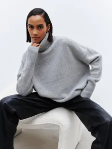 Detail view of a cozy grey turtleneck knit sweater worn by a model in a studio setup.