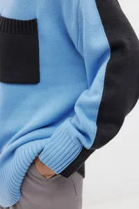 Close-up of blue and black color-blocked knit sweater with textured pocket and long sleeves.