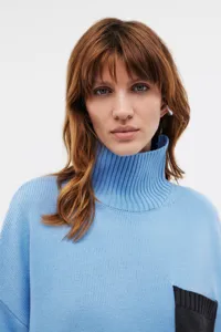 Close-up detail of soft blue turtleneck knit sweater with contrast black pocket accent.
