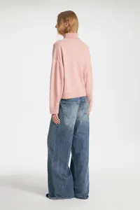 Back detail view of casual pink turtleneck knit sweater paired with baggy denim jeans.