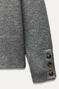 Grey knit sweater sleeve detail, ribbed cuff with three chic buttons, soft fabric texture.