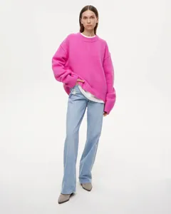 Detailed view of women's bright pink crewneck loose knit sweater worn with light blue jeans.