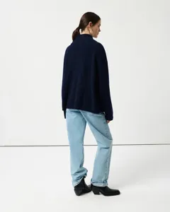 Detailed back view of women's dark blue high neck ribbed sweater paired with light blue jeans.
