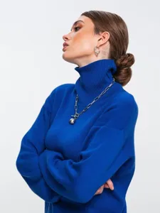 Detailed shot of a stylish blue turtleneck sweater featuring a chunky chain ball necklace.