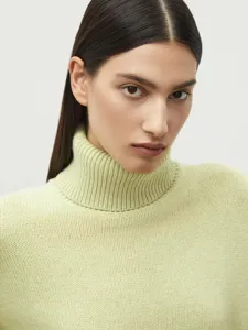 Close-up detail shot of a soft pastel green turtleneck knit sweater showcasing texture and fit.