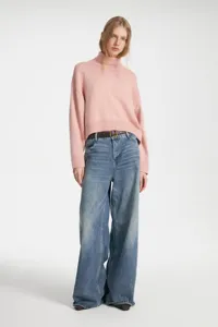 Detailed view of cozy pink turtleneck sweater paired with casual denim jeans and belt.