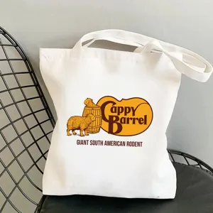 Close-up detail of white canvas tote bag with cute capybara graphic print on chair.