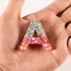 Resin letter pendant detail, epoxy handmade DIY keychain ornament showing glitter and pink stones.