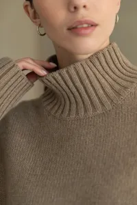 Close-up detail of women's ribbed turtleneck sweater in cozy khaki knit fabric texture.