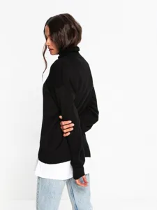 Detail shot of a black turtleneck sweater layered with white shirt and light denim jeans.