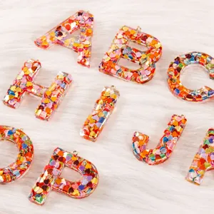Resin letter pendant detail, colorful heart glitter, DIY jewelry accessory, shiny finish.
