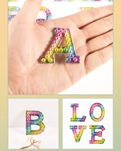 Close-up detail of colorful gradient rhinestone and pearl letter patch for DIY clothing accessories.