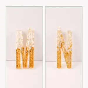 Close-up detail of resin alphabet letter M and N pendants with white stone and gold foil flakes.