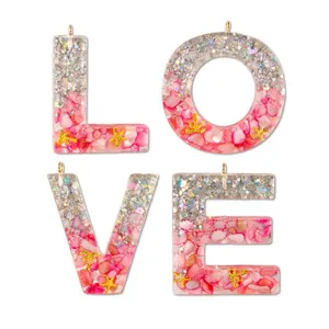Resin letter pendant detail view showing pink crushed stone and glitter inside transparent epoxy.