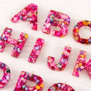 Detail shot of resin epoxy letter charm pendant embedded with pink crushed shell for DIY crafts.