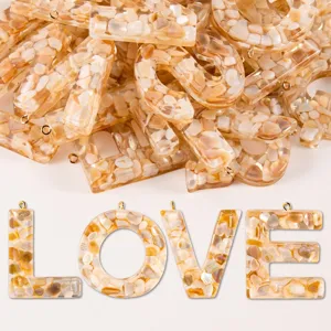 Close-up detail of resin letter charms filled with natural shell chips and gold rings.
