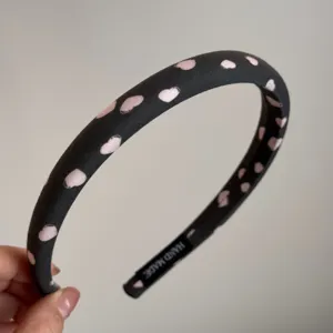 Detalle de diadema de tela negra con bonito estampado de corazones rosas, estilo artesanal.