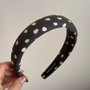 Diadema de tela negra con bonito patrón de corazones rosados y detalle de etiqueta artesanal