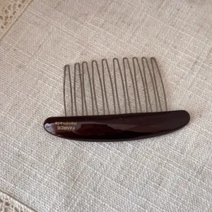 Close-up detail of dark brown acetate hair comb with metallic teeth, elegant and delicate accessory.