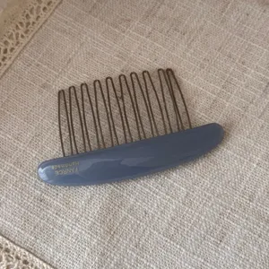 Detailed view of grey-blue acetate hair comb with metal teeth on textured fabric.