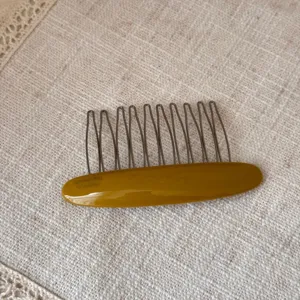 Detail shot of an elegant oval acetate hair comb featuring durable metal teeth on textured fabric.