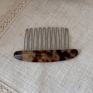 Close-up detail of tortoiseshell acetate hair comb with metal teeth on textured fabric background.