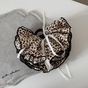 Primo piano di un fermaglio per capelli leopardato vintage con fiocchi bianchi e bordo nero.