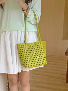Détail de sac cabas tissé en cuir vert, présentant une texture souple et des doubles anses.