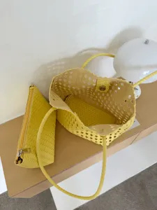 Détail de sac cabas ajouré en cuir tissé jaune avec design de panier creux et pochette assortie.