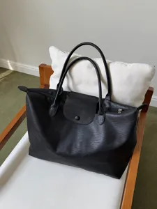 Detailansicht der schwarzen Shopper-Tasche mit klassischer Lederlasche und stabilen Griffen.
