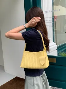 Detail shot of stylish yellow woven leather shoulder bag with chic handle and charm accessory.