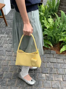 Yellow woven leather handbag detail shot showing intricate intrecciato texture and handle.