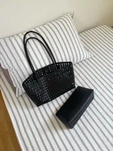 Detailed shot of a stylish black woven leather tote bag and matching pouch on striped bedding.