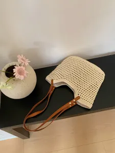 Detailed shot of a beige crochet tote bag with brown leather handles placed on a dark table.