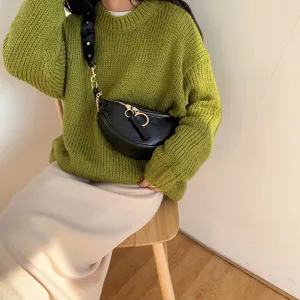 Detailed view of women fashion black crossbody waist bag with chain strap worn by model sitting.