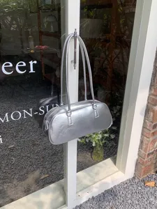 Detailed shot of a sleek silver metallic shoulder bag hanging on a glass door handle, minimalist.