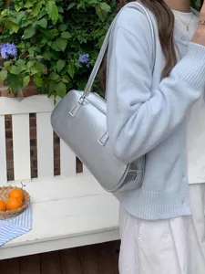 Detail shot showing the metallic silver shoulder bag worn by a model in a scenic outdoor setting.