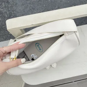 Detail view of a white soft leather crossbody bag with wide strap, showcasing interior space.
