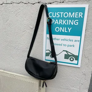Detail shot of a black soft leather shoulder bag with wide strap hanging against a textured wall.