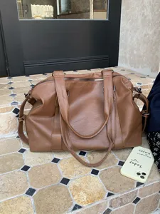 Brown leather travel duffel bag detail showing soft texture, double handles, and metal zippers.
