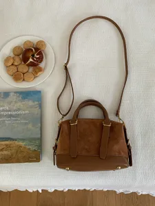 Close-up detail of retro brown suede shoulder bag, featuring dual handles and straps.