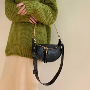 Detailed view of women's black leather crossbody chain bag worn with green knit sweater.