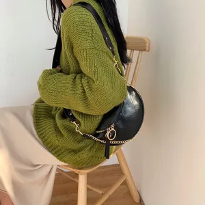 Close-up view of a stylish crescent shoulder bag with a gold chain strap and ring zipper.