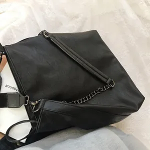 Black leather shoulder bag detail view, featuring chain strap and soft textured surface.