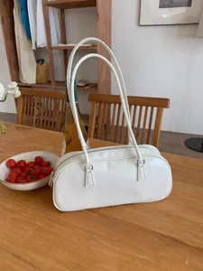 Close-up of a trendy white cylindrical shoulder bag on a wooden table, minimalist design detail.