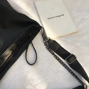 Detail view of black leather shoulder bag featuring metal chain strap and zipper close-up.