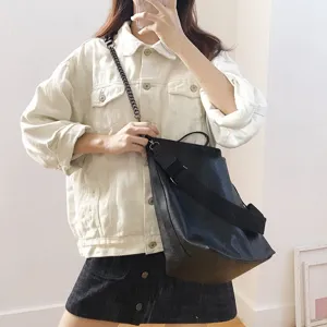 Detail view of the black bucket bag featuring a metal chain and wide strap, worn on shoulder.