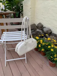Detailed view of the minimalist white shoulder bag hanging gracefully on an outdoor patio chair.